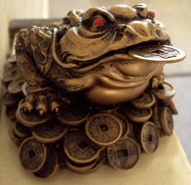 Gold resin three-legged toad figurine sitting on coins with a coin in its mouth and red gems for eyes