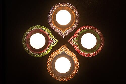 Small clay diya lamp with burning flame, surrounded by flower petals and gold coins