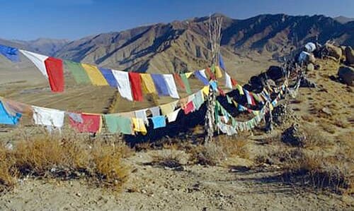 Colorful Tibetan prayer flags in five colors strung between mountain peaks with Himalayan backdrop