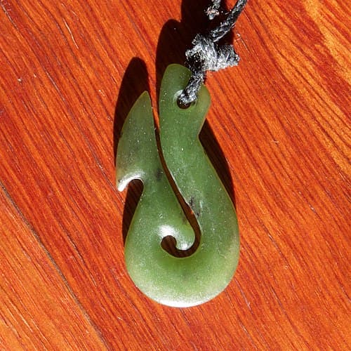 Polished bone Hei Matau fish hook pendant on a braided flaxen cord, with carved Maori surface decoration