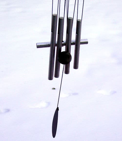 A set of silver metal wind chimes hanging from a decorative top piece, tubes of varying lengths producing gentle musical tones